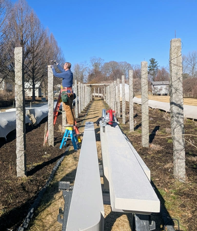 Beams and rafters painted Bedford Gray staged along the carriage road while Dmitri works from a ladder