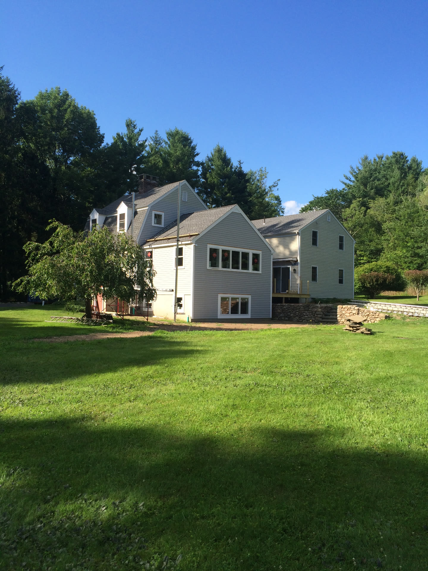 A renovated country house with new gabled addition, fresh siding, and stone retaining walls set on a wide lawn