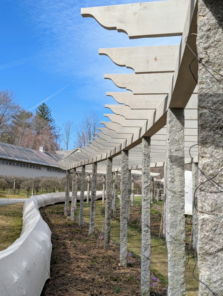 The restored 300-foot curved pergola at Martha Stewart's Bedford farm, with hand-cut cedar rafter tails resting on antique granite posts